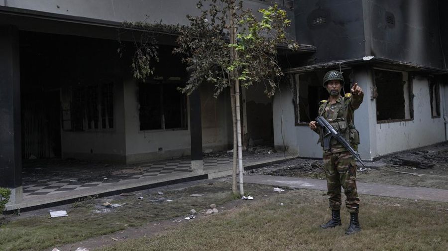 Para pengunjuk rasa antipemerintah berbaris menuju istana Perdana Menteri Sheikh Hasina sementara personel militer (tengah) berjaga di kawasan Shahbag, dekat Universitas Dhaka di Dhaka pada 5 Agustus 2024. Protes di Bangladesh yang dimulai sebagai demonstrasi yang dipimpin mahasiswa terhadap aturan perekrutan pemerintah pada bulan Juli mencapai puncaknya pada tanggal 5 Agustus, saat perdana menteri melarikan diri dan militer mengumumkan akan membentuk pemerintahan sementara. (Photo by Munir UZ ZAMAN / AFP)
