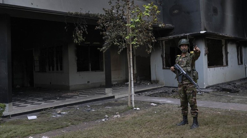 Para pengunjuk rasa antipemerintah berbaris menuju istana Perdana Menteri Sheikh Hasina sementara personel militer (tengah) berjaga di kawasan Shahbag, dekat Universitas Dhaka di Dhaka pada 5 Agustus 2024. Protes di Bangladesh yang dimulai sebagai demonstrasi yang dipimpin mahasiswa terhadap aturan perekrutan pemerintah pada bulan Juli mencapai puncaknya pada tanggal 5 Agustus, saat perdana menteri melarikan diri dan militer mengumumkan akan membentuk pemerintahan sementara. (Photo by Munir UZ ZAMAN / AFP)
