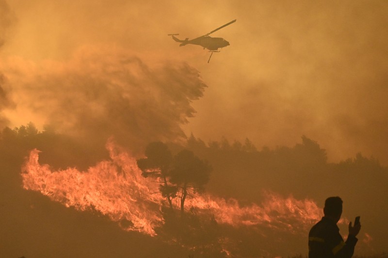 Penduduk setempat berdiri di samping mobil saat asap mengepul dari kebakaran hutan yang terjadi di desa Varnavas, dekat Athena, Yunani, 11 Agustus 2024. (REUTERS/Hilary Swift)