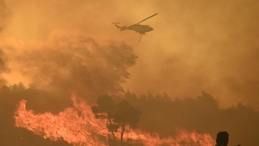 Penduduk setempat berdiri di samping mobil saat asap mengepul dari kebakaran hutan yang terjadi di desa Varnavas, dekat Athena, Yunani, 11 Agustus 2024. (REUTERS/Hilary Swift)