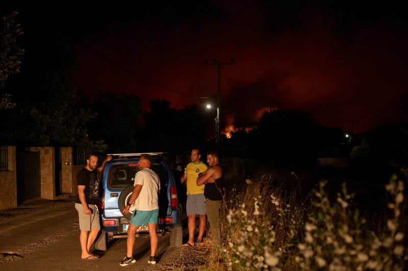Penduduk setempat berdiri di samping mobil saat asap mengepul dari kebakaran hutan yang terjadi di desa Varnavas, dekat Athena, Yunani, 11 Agustus 2024. Penduduk setempat berdiri di samping mobil saat asap mengepul dari kebakaran hutan yang terjadi di desa Varnavas, dekat Athena, Yunani, 11 Agustus 2024. (REUTERS/Hilary Swift)