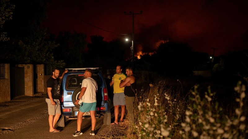 Penduduk setempat berdiri di samping mobil saat asap mengepul dari kebakaran hutan yang terjadi di desa Varnavas, dekat Athena, Yunani, 11 Agustus 2024. (REUTERS/Hilary Swift)
