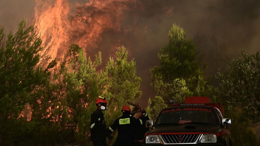 Penduduk setempat berdiri di samping mobil saat asap mengepul dari kebakaran hutan yang terjadi di desa Varnavas, dekat Athena, Yunani, 11 Agustus 2024. (REUTERS/Hilary Swift)