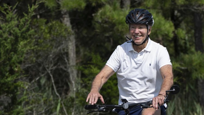 Presiden Joe Biden melambaikan tangan saat mengendarai sepedanya bersama agen Secret Service di Gordons Pond di Rehoboth Beach, Del., Minggu, 11 Agustus 2024. (AP Photo/Manuel Balce Ceneta)