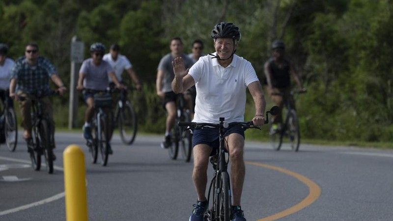 Presiden Joe Biden melambaikan tangan saat mengendarai sepedanya bersama agen Secret Service di Gordons Pond di Rehoboth Beach, Del., Minggu, 11 Agustus 2024. (AP Photo/Manuel Balce Ceneta)