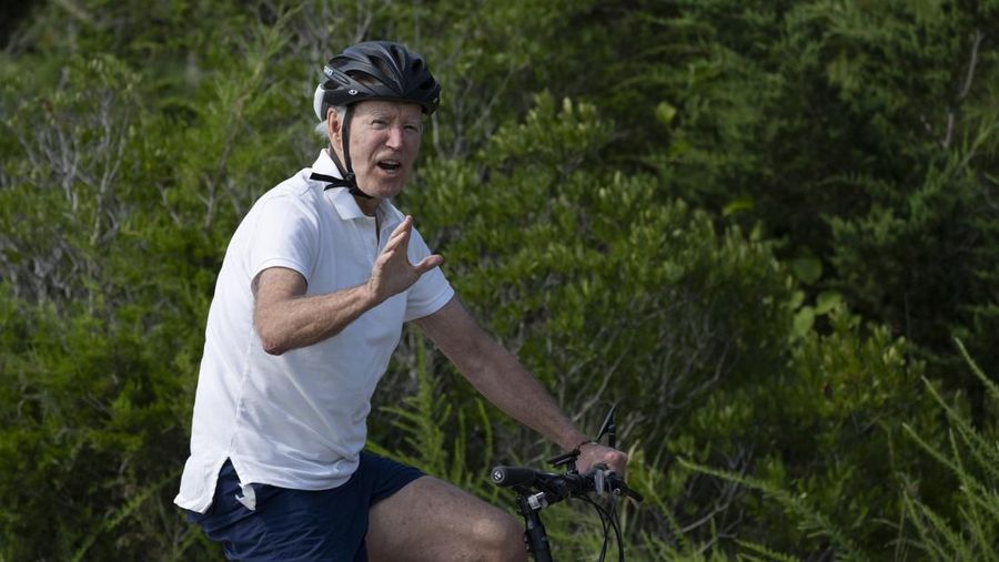 Presiden Joe Biden melambaikan tangan saat mengendarai sepedanya bersama agen Secret Service di Gordons Pond di Rehoboth Beach, Del., Minggu, 11 Agustus 2024. (AP Photo/Manuel Balce Ceneta)