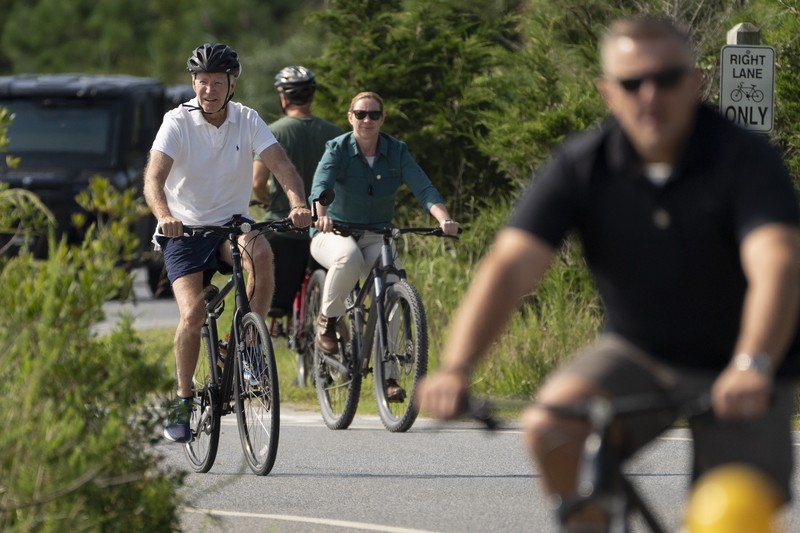 Presiden Joe Biden melambaikan tangan saat mengendarai sepedanya bersama agen Secret Service di Gordons Pond di Rehoboth Beach, Del., Minggu, 11 Agustus 2024. (AP Photo/Manuel Balce Ceneta)