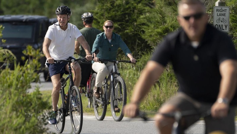 Presiden Joe Biden melambaikan tangan saat mengendarai sepedanya bersama agen Secret Service di Gordons Pond di Rehoboth Beach, Del., Minggu, 11 Agustus 2024. (AP Photo/Manuel Balce Ceneta)