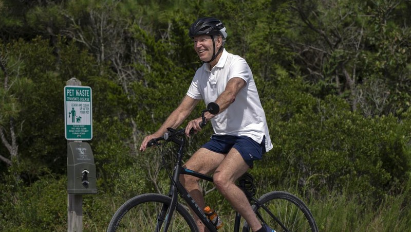 Presiden Joe Biden melambaikan tangan saat mengendarai sepedanya bersama agen Secret Service di Gordons Pond di Rehoboth Beach, Del., Minggu, 11 Agustus 2024. (AP Photo/Manuel Balce Ceneta)