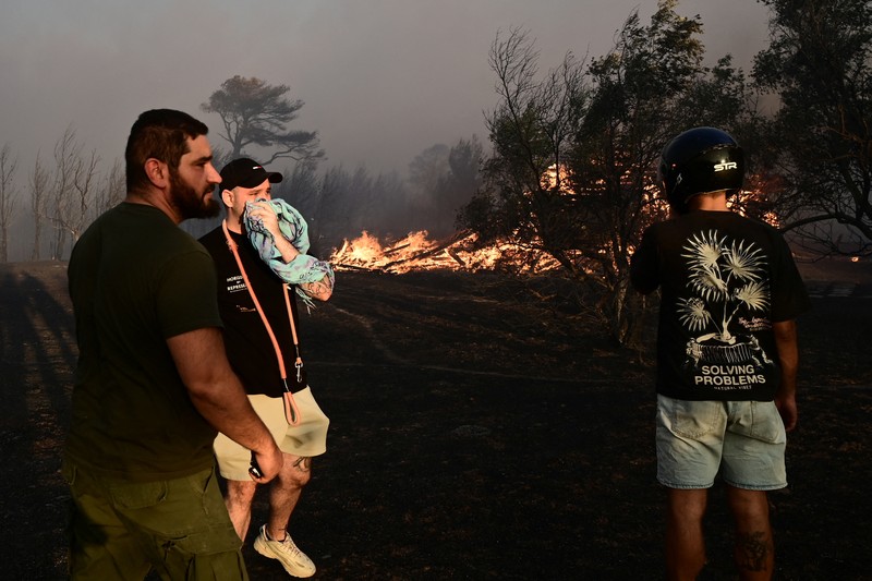 Penduduk setempat berdiri di samping mobil saat asap mengepul dari kebakaran hutan yang terjadi di desa Varnavas, dekat Athena, Yunani, 11 Agustus 2024. Penduduk setempat berdiri di samping mobil saat asap mengepul dari kebakaran hutan yang terjadi di desa Varnavas, dekat Athena, Yunani, 11 Agustus 2024. (REUTERS/Hilary Swift)