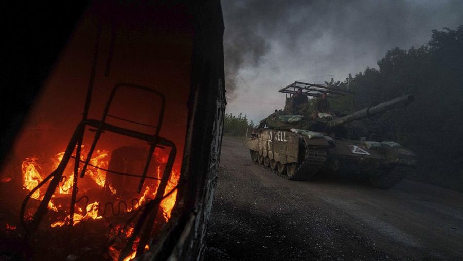A Ukrainian tank passes by a burning car near the Russian-Ukrainian border, Sumy region, Ukraine, Wednesday, Aug. 14, 2024. (AP Photo/Evgeniy Maloletka)