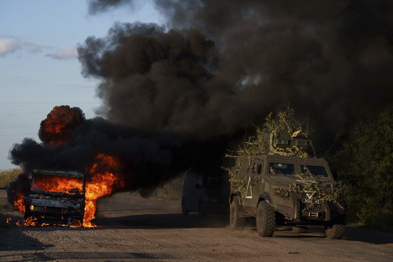 A Ukrainian tank passes by a burning car near the Russian-Ukrainian border, Sumy region, Ukraine, Wednesday, Aug. 14, 2024. (AP Photo/Evgeniy Maloletka)