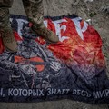 Seorang prajurit Ukraina berdiri di atas bendera kelompok tentara bayaran Rusia Wagner, di tengah serangan Rusia terhadap Ukraina, dekat perbatasan Rusia di wilayah Sumy, Ukraina, 13 Agustus 2024. (REUTERS/Viacheslav Ratynsky)