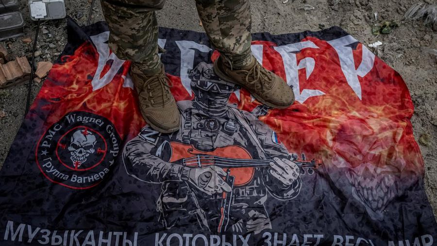 Seorang prajurit Ukraina berdiri di atas bendera kelompok tentara bayaran Rusia Wagner, di tengah serangan Rusia terhadap Ukraina, dekat perbatasan Rusia di wilayah Sumy, Ukraina, 13 Agustus 2024. (REUTERS/Viacheslav Ratynsky)