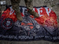 Seorang prajurit Ukraina berdiri di atas bendera kelompok tentara bayaran Rusia Wagner, di tengah serangan Rusia terhadap Ukraina, dekat perbatasan Rusia di wilayah Sumy, Ukraina, 13 Agustus 2024. (REUTERS/Viacheslav Ratynsky)