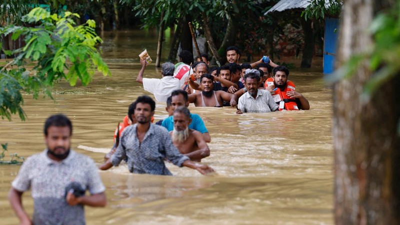Orang-orang membawa barang-barang mereka untuk menyeberangi jalan yang banjir setelah hujan lebat di Ahmedabad, India, 28 Agustus 2024. (REUTERS/Amit Dave)