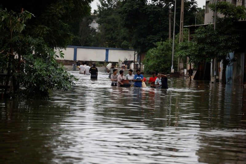 Orang-orang membawa barang-barang mereka untuk menyeberangi jalan yang banjir setelah hujan lebat di Ahmedabad, India, 28 Agustus 2024. Orang-orang membawa barang-barang mereka untuk menyeberangi jalan yang banjir setelah hujan lebat di Ahmedabad, India, 28 Agustus 2024. (REUTERS/Amit Dave)