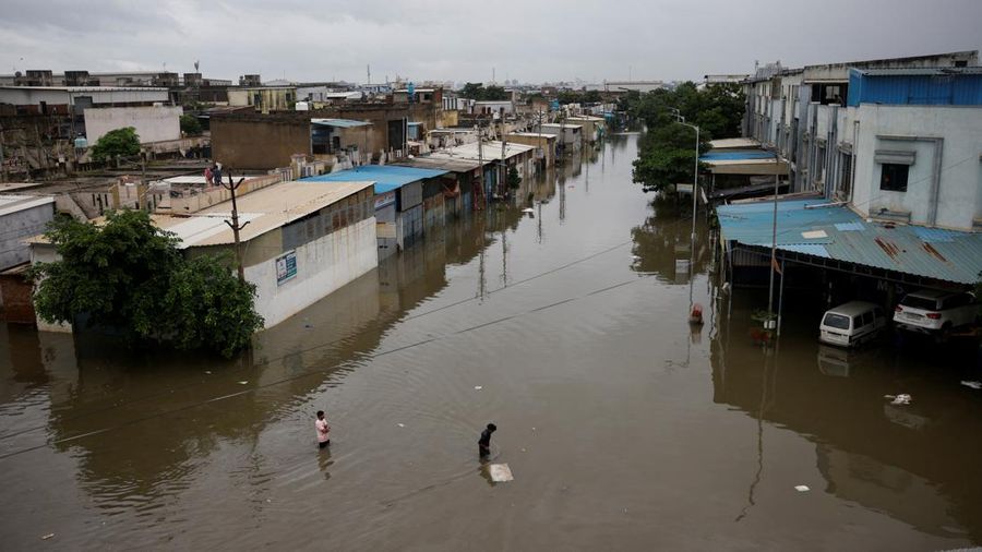 Orang-orang membawa barang-barang mereka untuk menyeberangi jalan yang banjir setelah hujan lebat di Ahmedabad, India, 28 Agustus 2024. (REUTERS/Amit Dave)
