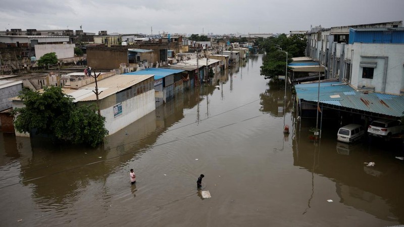 Orang-orang membawa barang-barang mereka untuk menyeberangi jalan yang banjir setelah hujan lebat di Ahmedabad, India, 28 Agustus 2024. (REUTERS/Amit Dave)
