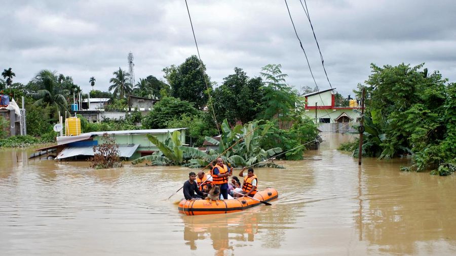 Orang-orang membawa barang-barang mereka untuk menyeberangi jalan yang banjir setelah hujan lebat di Ahmedabad, India, 28 Agustus 2024. (REUTERS/Amit Dave)