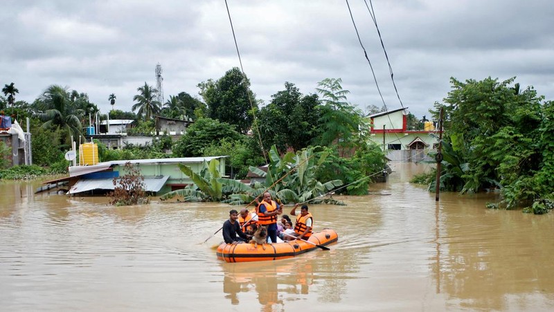Orang-orang membawa barang-barang mereka untuk menyeberangi jalan yang banjir setelah hujan lebat di Ahmedabad, India, 28 Agustus 2024. (REUTERS/Amit Dave)