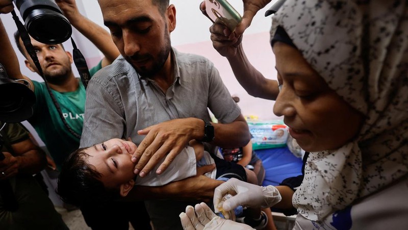 Seorang pria Palestina menggendong seorang anak, saat anak tersebut divaksinasi polio, di tengah konflik Israel-Hamas, di rumah sakit Nasser di Khan Younis di Jalur Gaza selatan, 31 Agustus 2024. (REUTERS/Mohammed Salem)