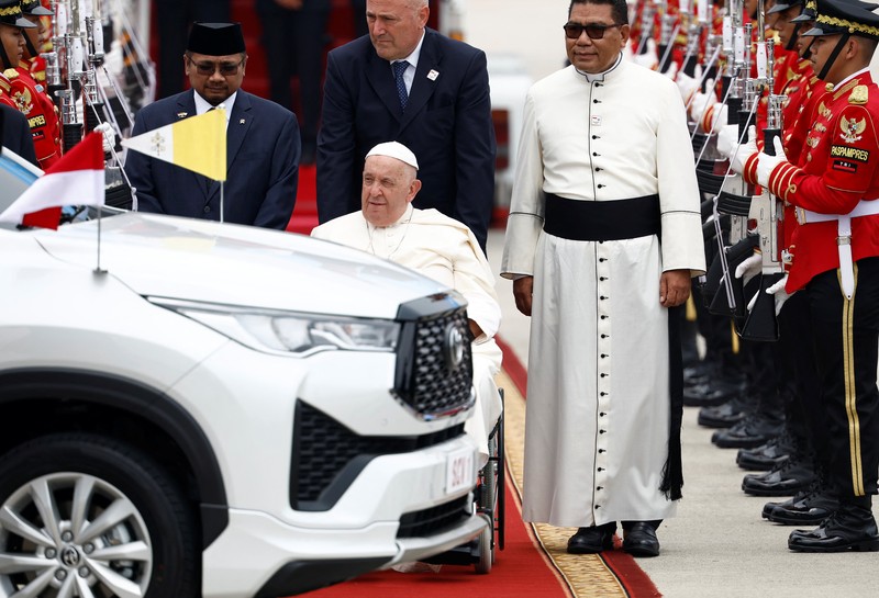 Paus Fransiskus di kursi rodanya, melambaikan tangan saat tiba selama upacara penyambutan resmi di Bandara Internasional Soekarno-Hatta di Tangerang di pinggiran Jakarta, Indonesia, Selasa, 3 September 2024. (AP Photo/Achmad Ibrahim)