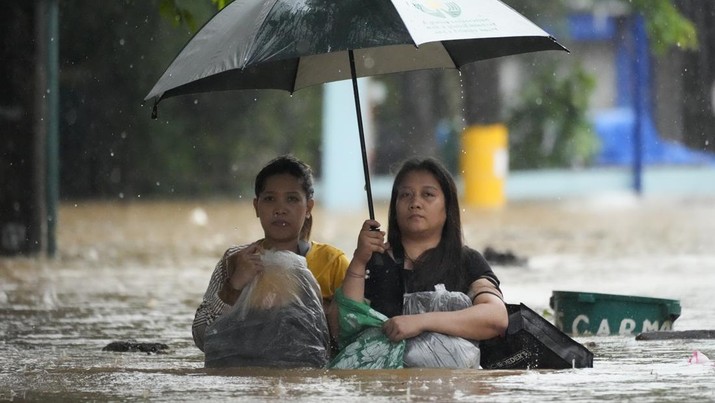 Warga melindungi barang-barang mereka saat melewati jalan yang banjir akibat hujan lebat akibat Badai Tropis Yagi, yang secara lokal disebut Enteng, di Cainta, provinsi Rizal, Filipina, Senin, 2 September 2024. (AP Photo/Aaron Favila)