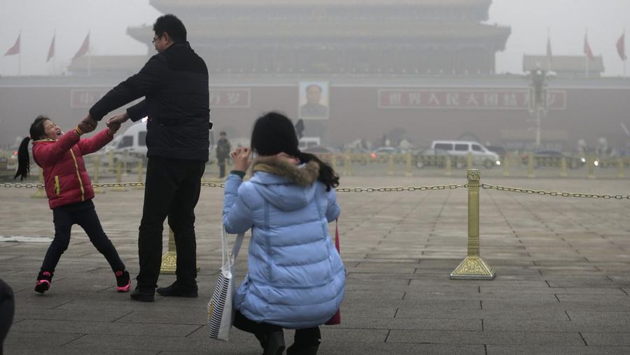 A woman takes picture of her husband and their child playing on Tiananmen Square on a heavily polluted day in Beijing, Tuesday, Dec. 1, 2015. Schools in the Chinese capital kept students indoors and parents brought their kids to hospitals with breathing ailments Tuesday as Beijing grappled with extremely severe air pollution for the fifth straight day. (AP Photo/Andy Wong)