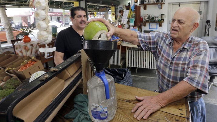 In this photo taken Tuesday, June 9, 2015, Angel Hernandez, fruit store owner, right, pours coconut water in a bottle for customer Jorge Ocuriz, left, at a local fruit store in the Little Havana area of Miami. (AP Photo/Alan Diaz)