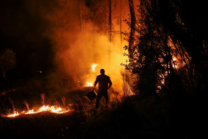 Seorang pria memegang ember selama kebakaran hutan di Nelas, Portugal, 16 September 2024. (REUTERS/Pedro Nunes)