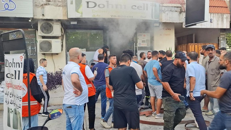 Orang-orang berkumpul saat asap mengepul dari sebuah toko keliling di Sidon, Lebanon, 18 September 2024. (REUTERS/Hassan Hankir)