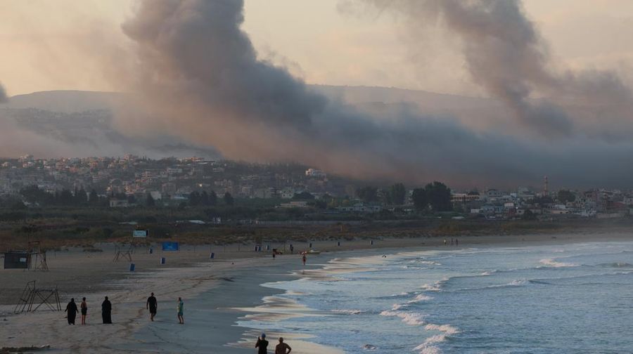 People walk at a beach as smoke billows over southern Lebanon following Israeli strikes, amid ongoing cross-border hostilities between Hezbollah and Israeli forces, as seen from Tyre, southern Lebanon September 23, 2024. REUTERS/Aziz Taher