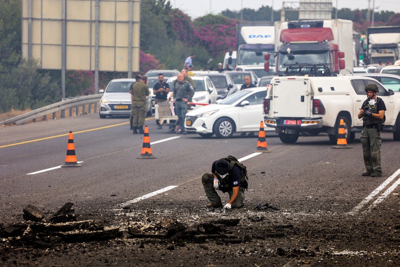 Petugas keamanan menangani sisa-sisa serangan roket kelompok Hizbullah yang mendarat pada jalan raya di Kfar Qasim, Israel, Selasa (1/10/2024). (REUTERS/Moti Milrod)