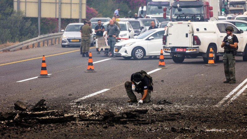 Petugas keamanan menangani sisa-sisa serangan roket kelompok Hizbullah yang mendarat pada jalan raya di Kfar Qasim, Israel, Selasa (1/10/2024). (REUTERS/Moti Milrod)