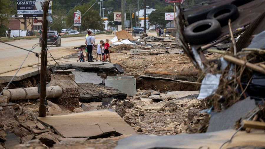 Warga Swannanoa berjalan melewati kerusakan akibat banjir dahsyat dari Sungai Swannanoa. Sisa Badai Helene menyebabkan banjir besar, pohon tumbang, dan pemadaman listrik di wilayah barat Carolina Utara, AS, 29 September 2024. (Travis Long/ The News & Observer/Handout via REUTERS)
