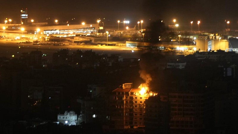 Api dan asap mengepul dari sebuah gedung yang terkena serangan udara Israel di Dahiyeh, sementara Bandara Internasional Rafik Hariri terlihat di latar belakang, di Beirut, Lebanon, Jumat, 4 Oktober 2024. (AP Photo/Hussein Malla)