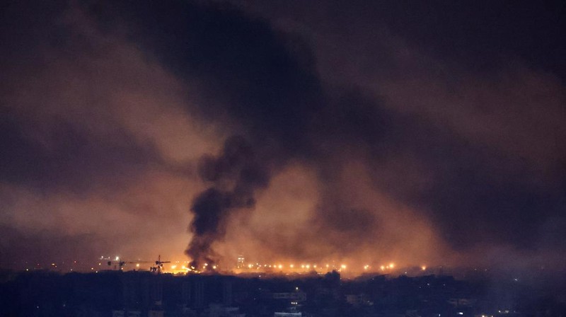 Api dan asap mengepul dari sebuah gedung yang terkena serangan udara Israel di Dahiyeh, sementara Bandara Internasional Rafik Hariri terlihat di latar belakang, di Beirut, Lebanon, Jumat, 4 Oktober 2024. (AP Photo/Hussein Malla)