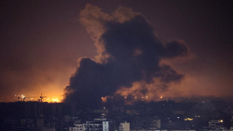 Api dan asap mengepul dari sebuah gedung yang terkena serangan udara Israel di Dahiyeh, sementara Bandara Internasional Rafik Hariri terlihat di latar belakang, di Beirut, Lebanon, Jumat, 4 Oktober 2024. (AP Photo/Hussein Malla)