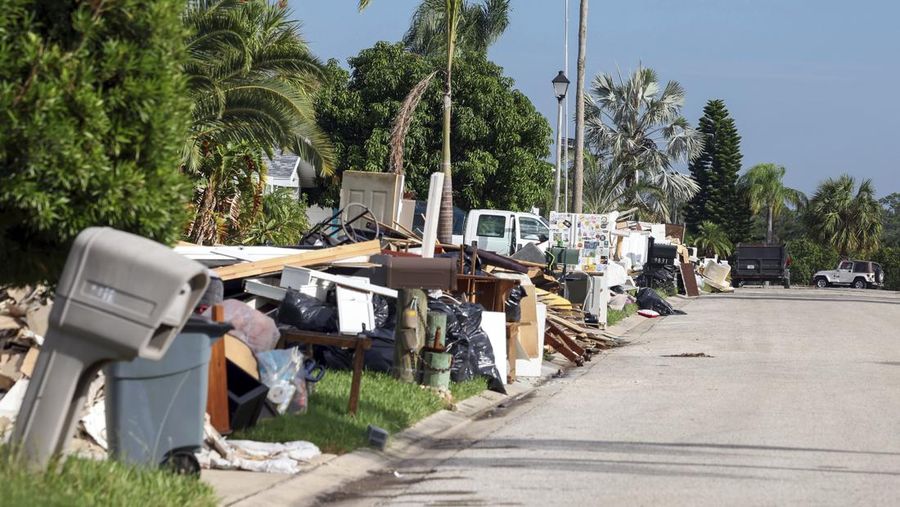 A tattered American flag flaps outside a home as furniture and household items damaged by Hurricane Helene flooding sit piled along the street awaiting pickup, ahead of the arrival of Hurricane Milton, in Holmes Beach on Anna Maria Island, Fla., Tuesday, Oct. 8, 2024. (AP Photo/Rebecca Blackwell)