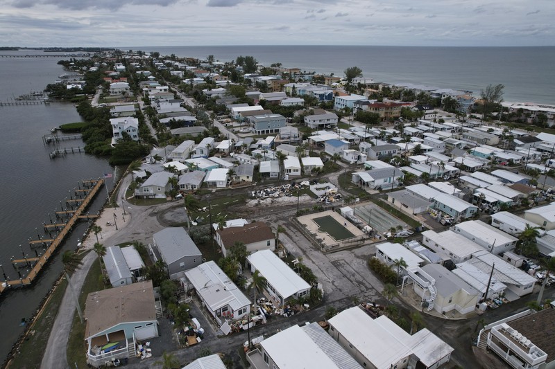 A tattered American flag flaps outside a home as furniture and household items damaged by Hurricane Helene flooding sit piled along the street awaiting pickup, ahead of the arrival of Hurricane Milton, in Holmes Beach on Anna Maria Island, Fla., Tuesday, Oct. 8, 2024. (AP Photo/Rebecca Blackwell)