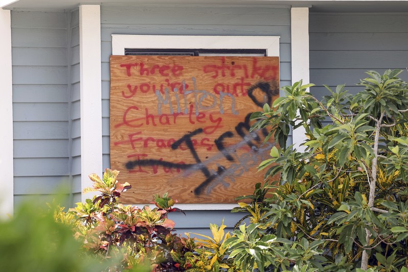 A tattered American flag flaps outside a home as furniture and household items damaged by Hurricane Helene flooding sit piled along the street awaiting pickup, ahead of the arrival of Hurricane Milton, in Holmes Beach on Anna Maria Island, Fla., Tuesday, Oct. 8, 2024. (AP Photo/Rebecca Blackwell)