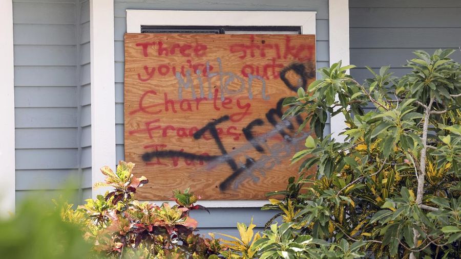 A tattered American flag flaps outside a home as furniture and household items damaged by Hurricane Helene flooding sit piled along the street awaiting pickup, ahead of the arrival of Hurricane Milton, in Holmes Beach on Anna Maria Island, Fla., Tuesday, Oct. 8, 2024. (AP Photo/Rebecca Blackwell)