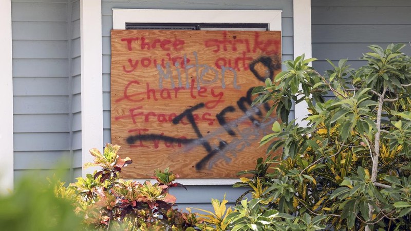 A tattered American flag flaps outside a home as furniture and household items damaged by Hurricane Helene flooding sit piled along the street awaiting pickup, ahead of the arrival of Hurricane Milton, in Holmes Beach on Anna Maria Island, Fla., Tuesday, Oct. 8, 2024. (AP Photo/Rebecca Blackwell)