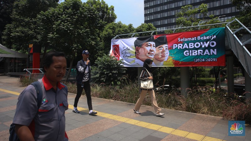 Warga berjalan di dekat spanduk bertuliskan 'Selamat Bekerja Prabowo-Gibran' di Jakarta, Kamis (17/10/2024). (CNBC Indonesia/Faisal Rahman)