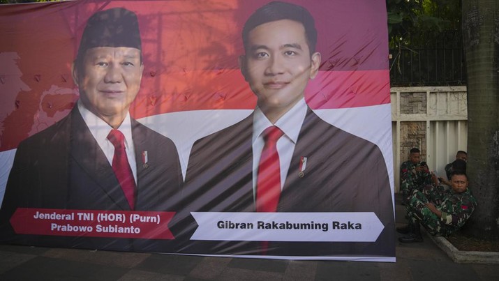 Soldiers sit next to a banner showing Indonesian President-elect Prabowo Subianto, left, and Vice President-elect Gibran Rakabuming Raka, who is also the eldest son of outgoing President Joko Widodo in Jakarta, Indonesia, Sunday, Oct. 20, 2024. (AP Photo/Dita Alangkara)