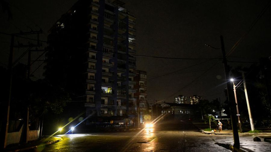Seorang wanita sedang berjalan-jalan dengan anjingnya di dekat lampu jalan saat pemerintah Kuba mengatakan pada hari Sabtu bahwa mereka telah membuat beberapa kemajuan dalam membangun kembali layanan listrik secara bertahap di seluruh pulau, di Havana, Kuba, 19 Oktober 2024. (REUTERS/Norlys Perez)