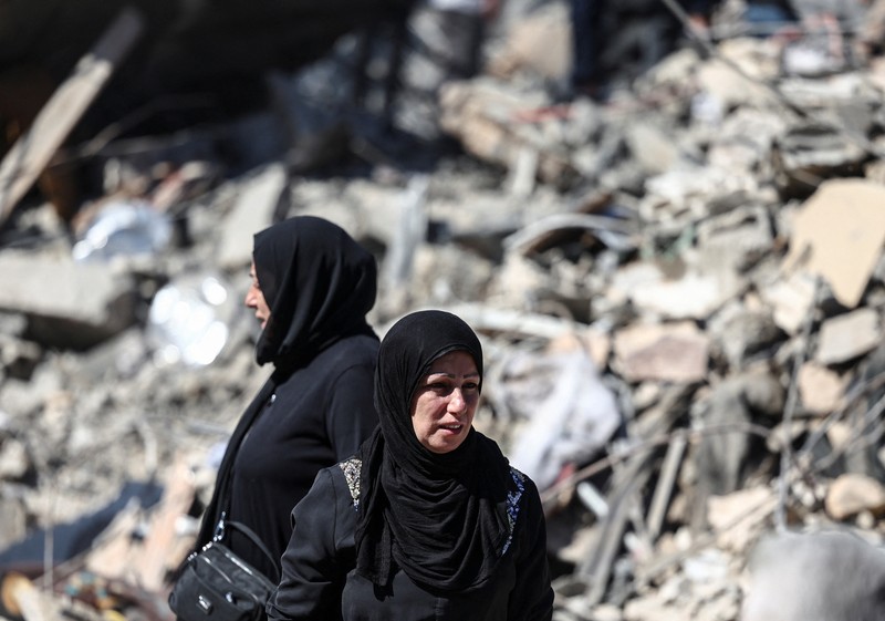 Orang-orang berdiri di atas reruntuhan bangunan yang dihancurkan setelah serangan Israel di dekat Rumah Sakit Universitas Rafik Hariri, di tengah permusuhan yang sedang berlangsung antara Hizbullah dan pasukan Israel, di Beirut, Lebanon, 22 Oktober 2024. (REUTERS/Yara Nardi)