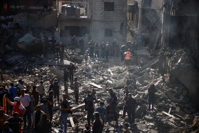 Orang-orang berdiri di atas reruntuhan bangunan yang dihancurkan setelah serangan Israel di dekat Rumah Sakit Universitas Rafik Hariri, di tengah permusuhan yang sedang berlangsung antara Hizbullah dan pasukan Israel, di Beirut, Lebanon, 22 Oktober 2024. (REUTERS/Yara Nardi)