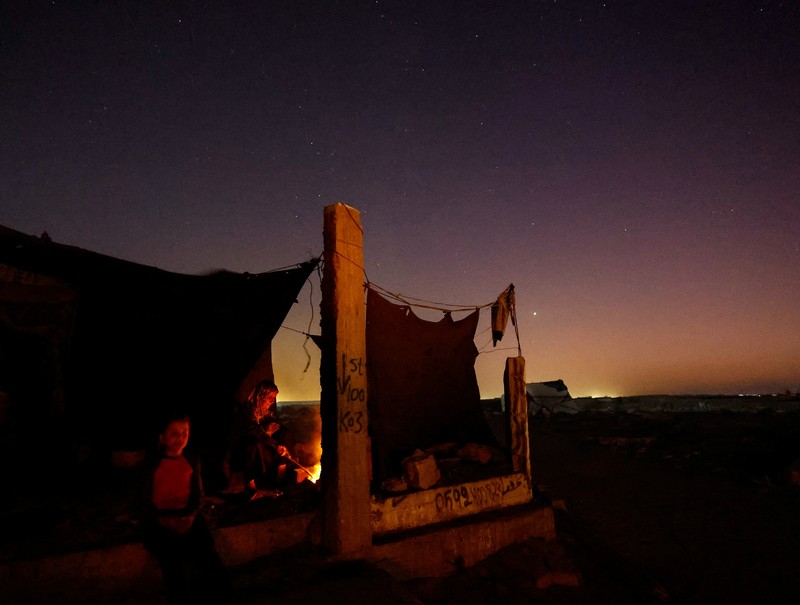 Warga Palestina yang mengungsi menyalakan api di tenda mereka saat mereka tinggal di pemakaman, di tengah konflik Israel-Hamas, di Khan Younis, di Jalur Gaza selatan, 27 Oktober 2024. (REUTERS/Mohammed Salem)